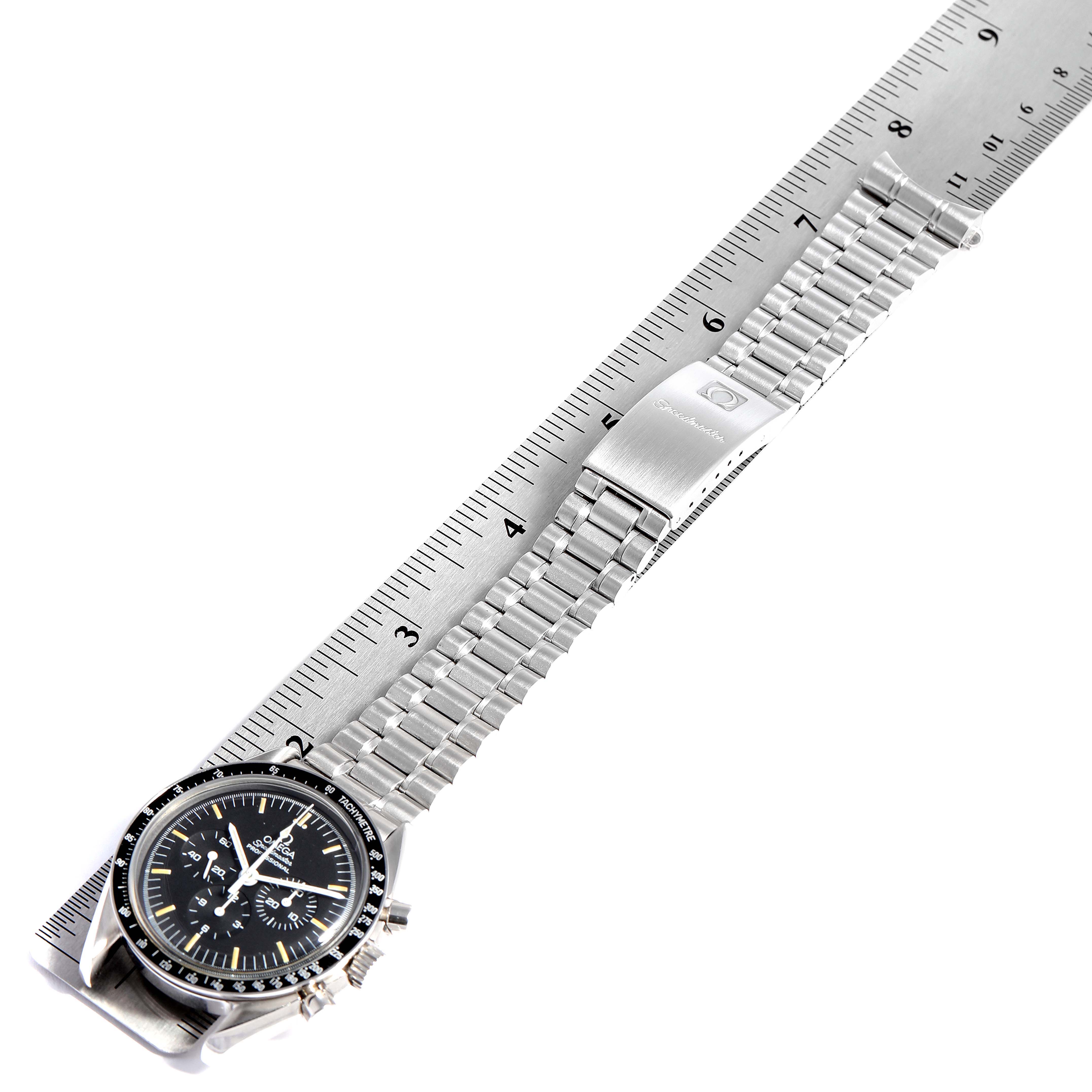 The image shows the Omega Speedmaster 3592.50.00 Men
s Stainless Steel Black Dial 3592.50.00 Men
s Stainless Steel Black Dial watch and its metal bracelet laid flat on a ruler, displaying the case and clasp.