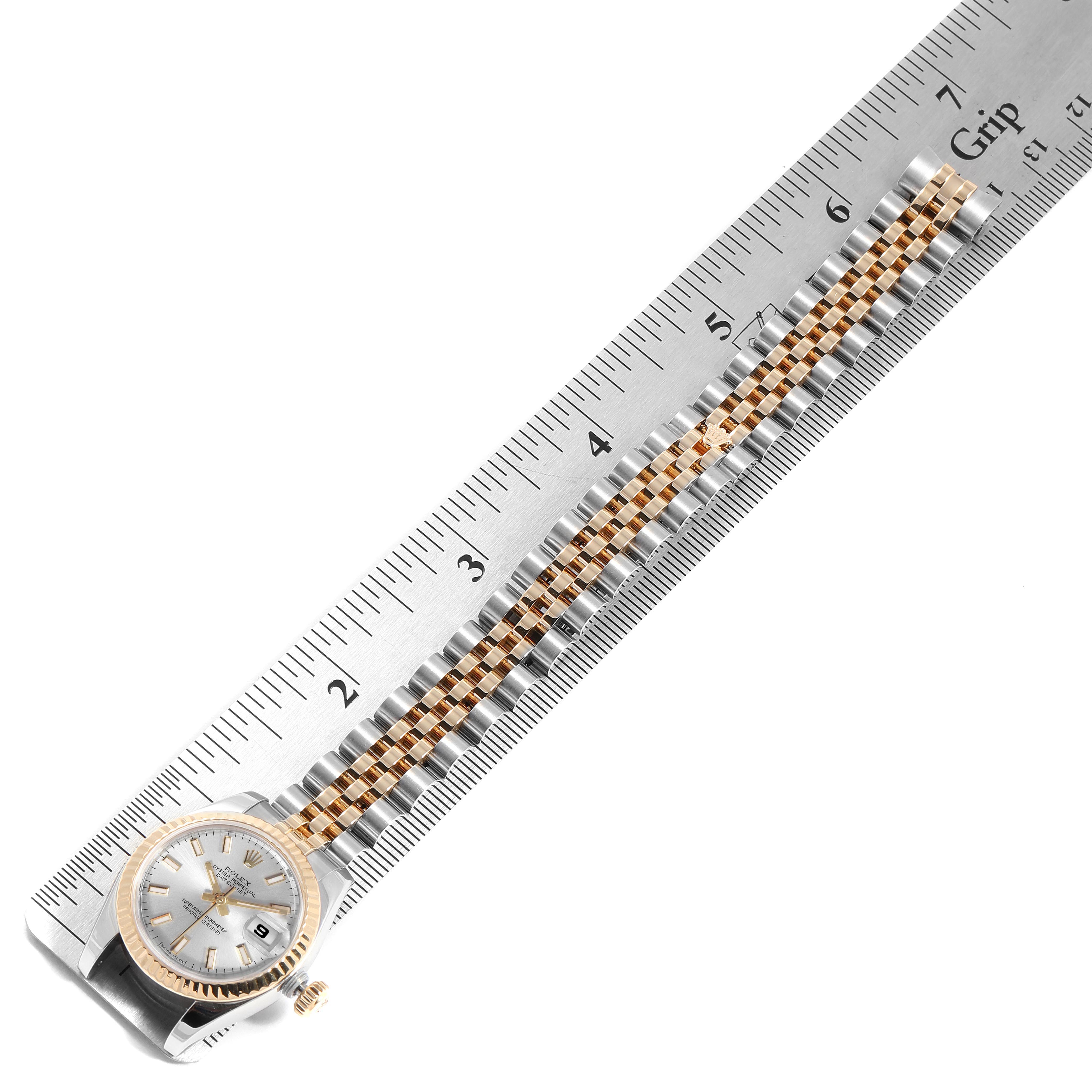 The Rolex Datejust 179173 Women's Steel and Gold (two tone) Silver Dial 179173 Women's Steel and Gold (two tone) Silver Dial watch is shown from an angled top view, highlighting the face and metal bracelet alongside a ruler.