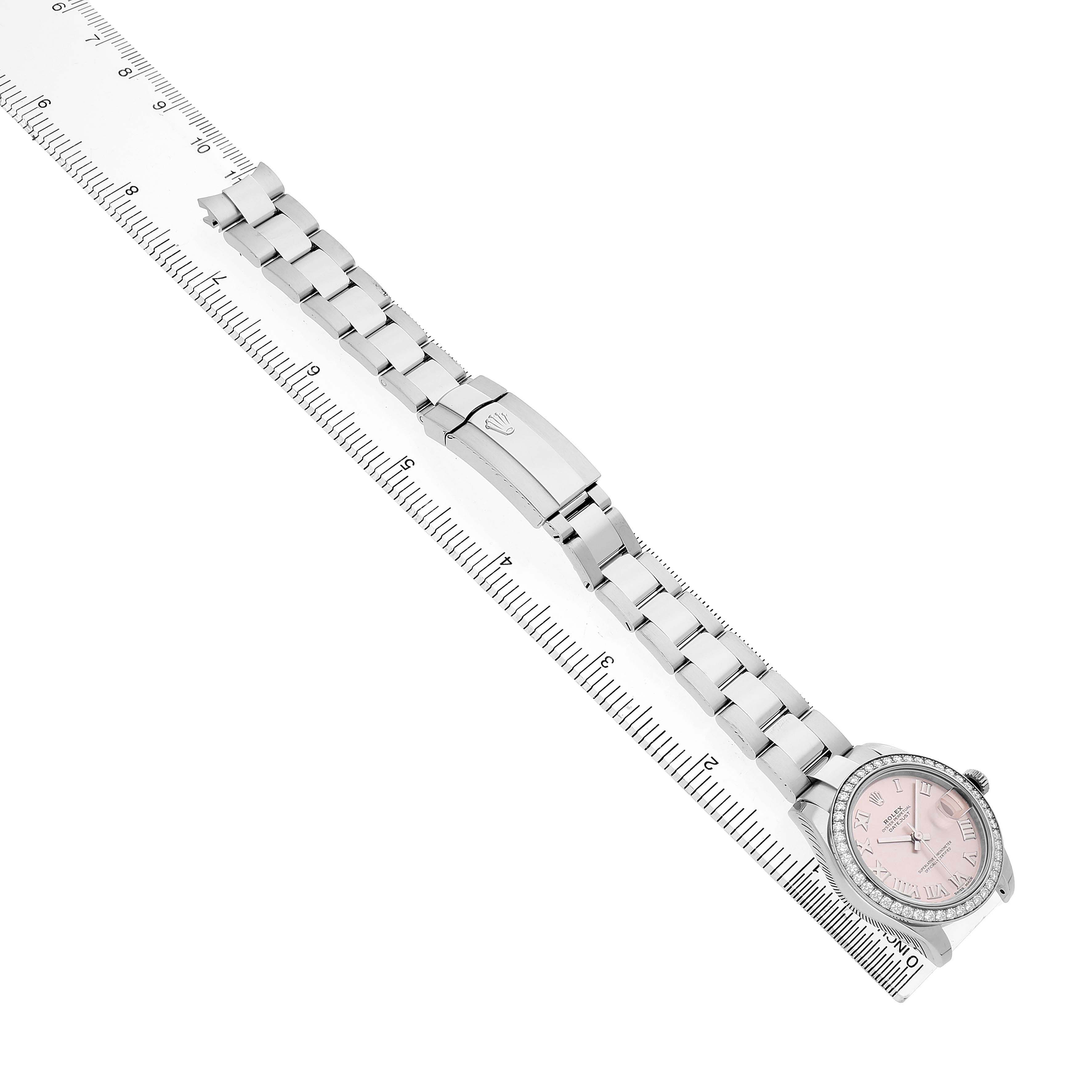 The Rolex Datejust 178384 Women's Stainless Steel Pink Dial watch is shown from a top-down angle, highlighting the bracelet, clasp, and dial beside a ruler.
