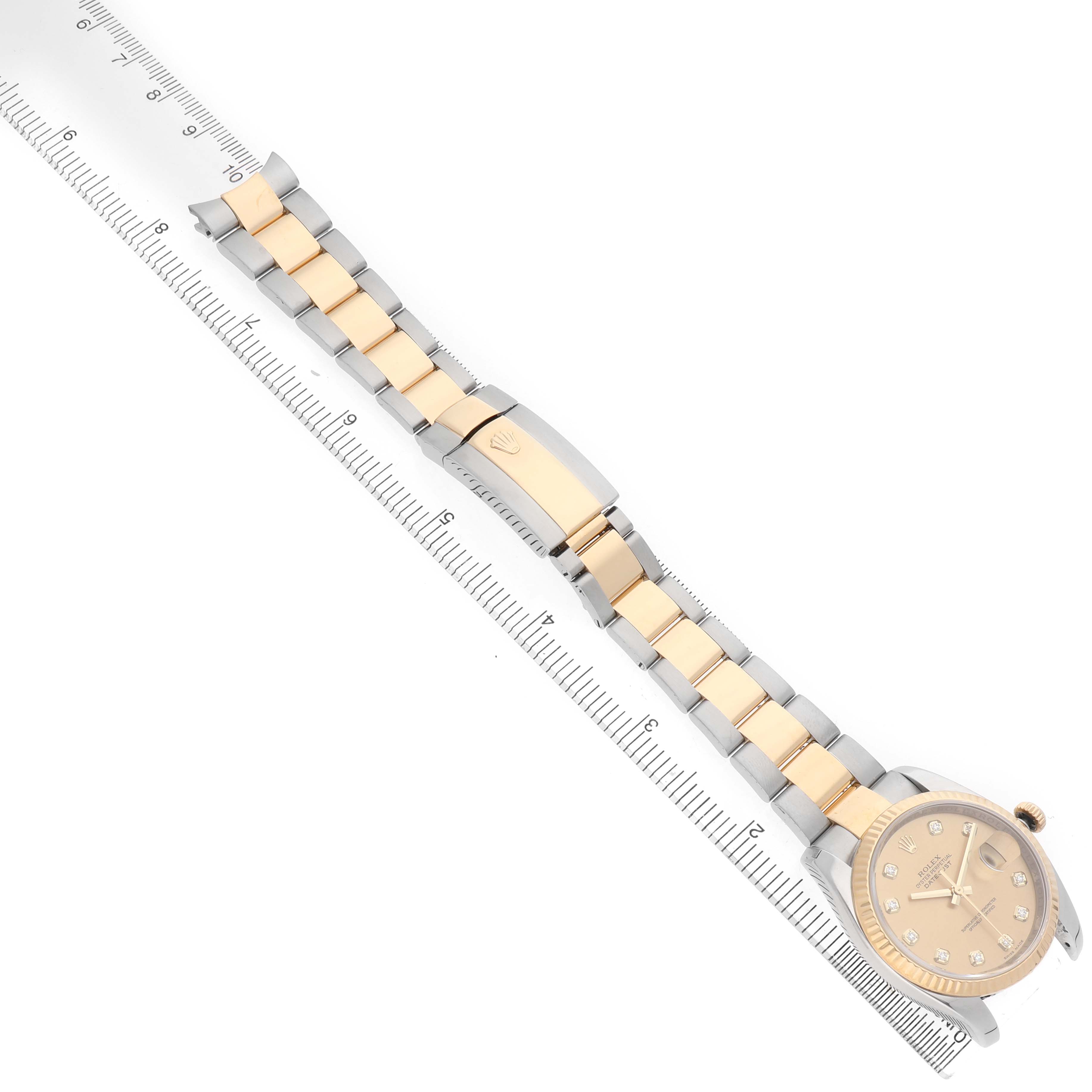 The Rolex Datejust 116233 Men's Steel and Gold (two tone) Champagne Dial watch is shown from an overhead angle, revealing the dial, bracelet, and clasp, alongside a ruler for scale.