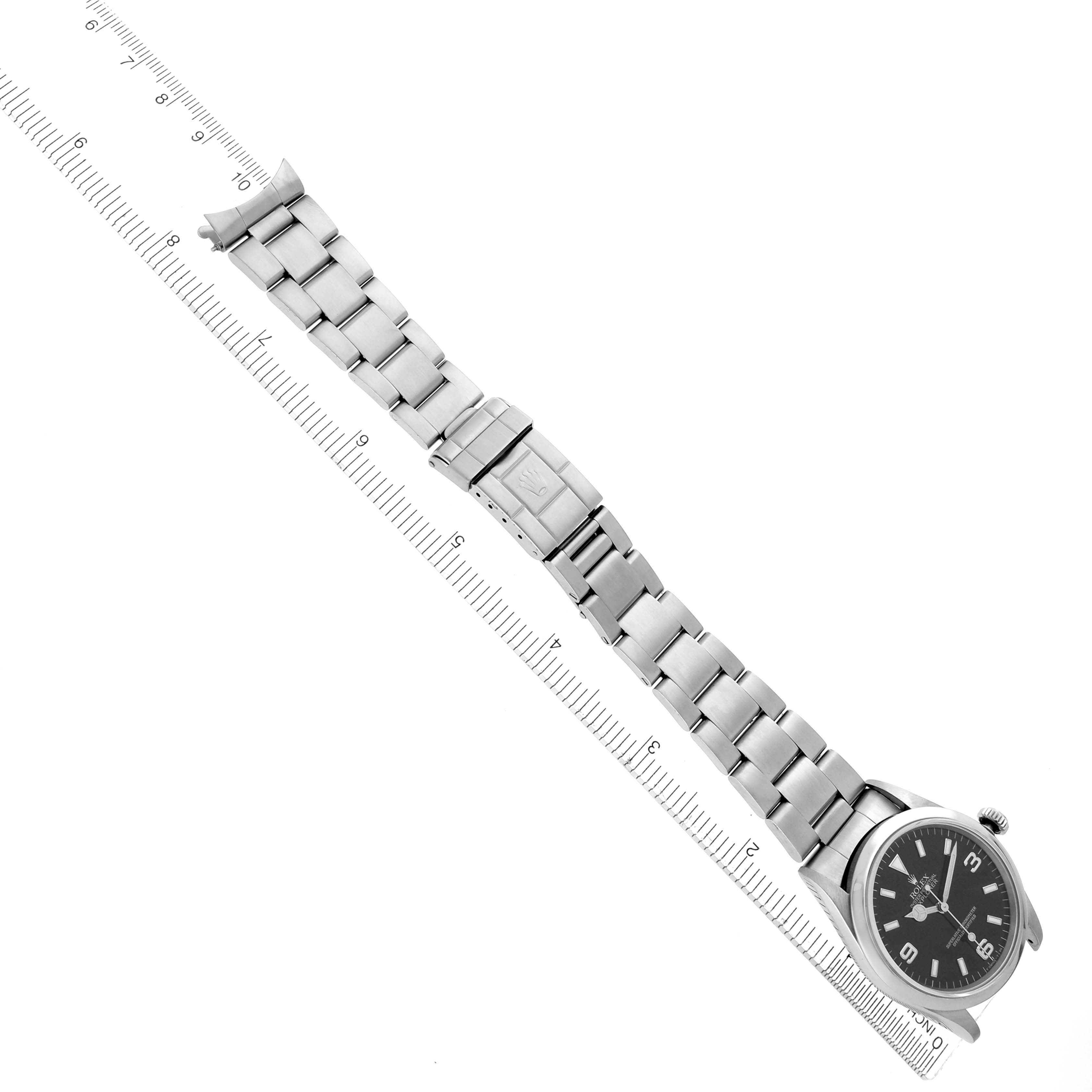 The Rolex Explorer 14270 Men
s Stainless Steel Black Dial 14270 Men
s Stainless Steel Black Dial watch is shown from a top-down angle, displaying the bracelet, clasp, and face alongside a ruler.