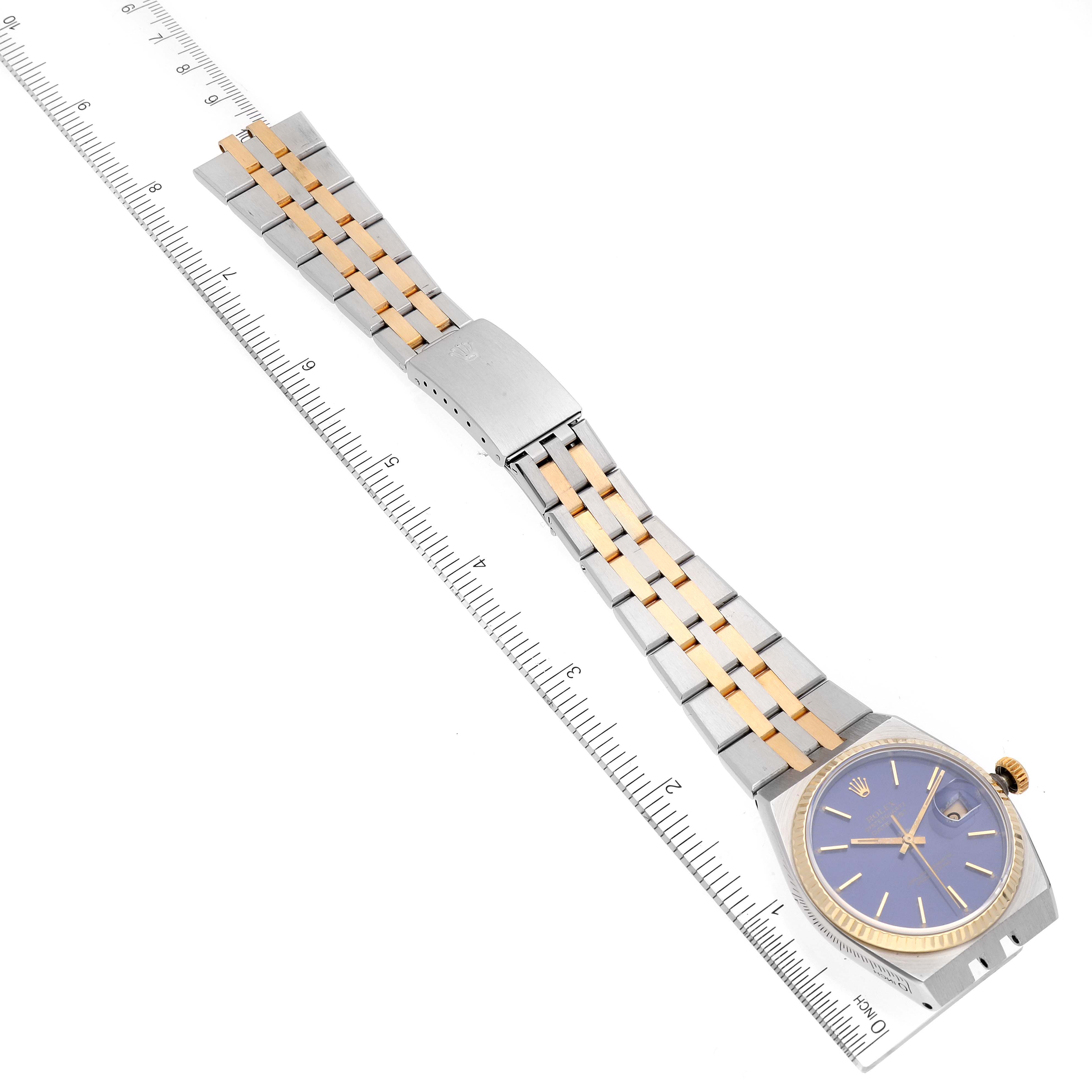 The Rolex Oysterquartz 17013 Men's Steel and Gold (two tone) Blue Dial 17013 Men's Steel and Gold (two tone) Blue Dial watch is shown from an overhead angle, displaying its face, case, and two-tone bracelet next to a ruler.