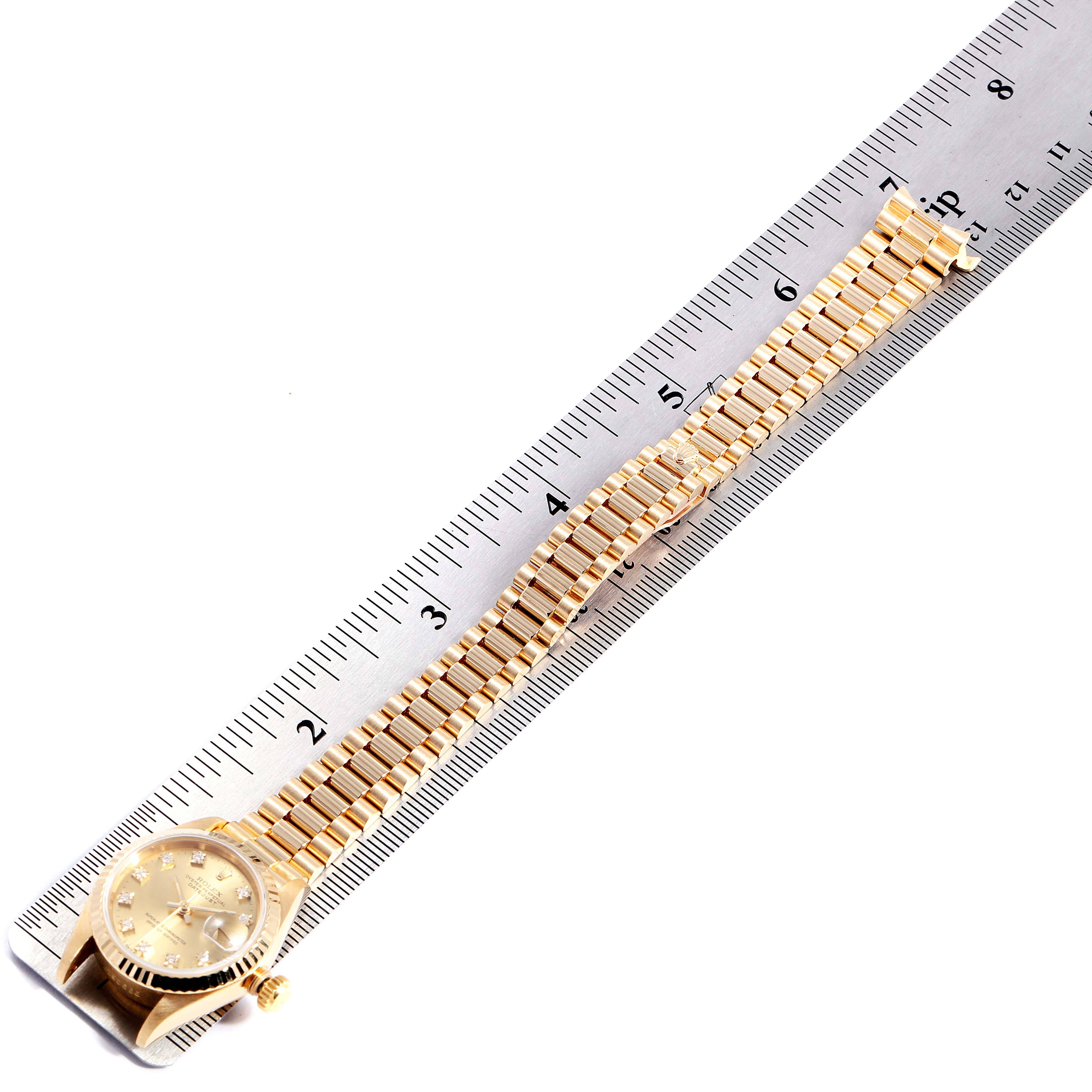 This image shows a gold Rolex President 69178 Women
s Yellow Gold Champagne Dial 69178 Women
s Yellow Gold Champagne Dial model watch laid flat on a ruler, displaying the band and dial.