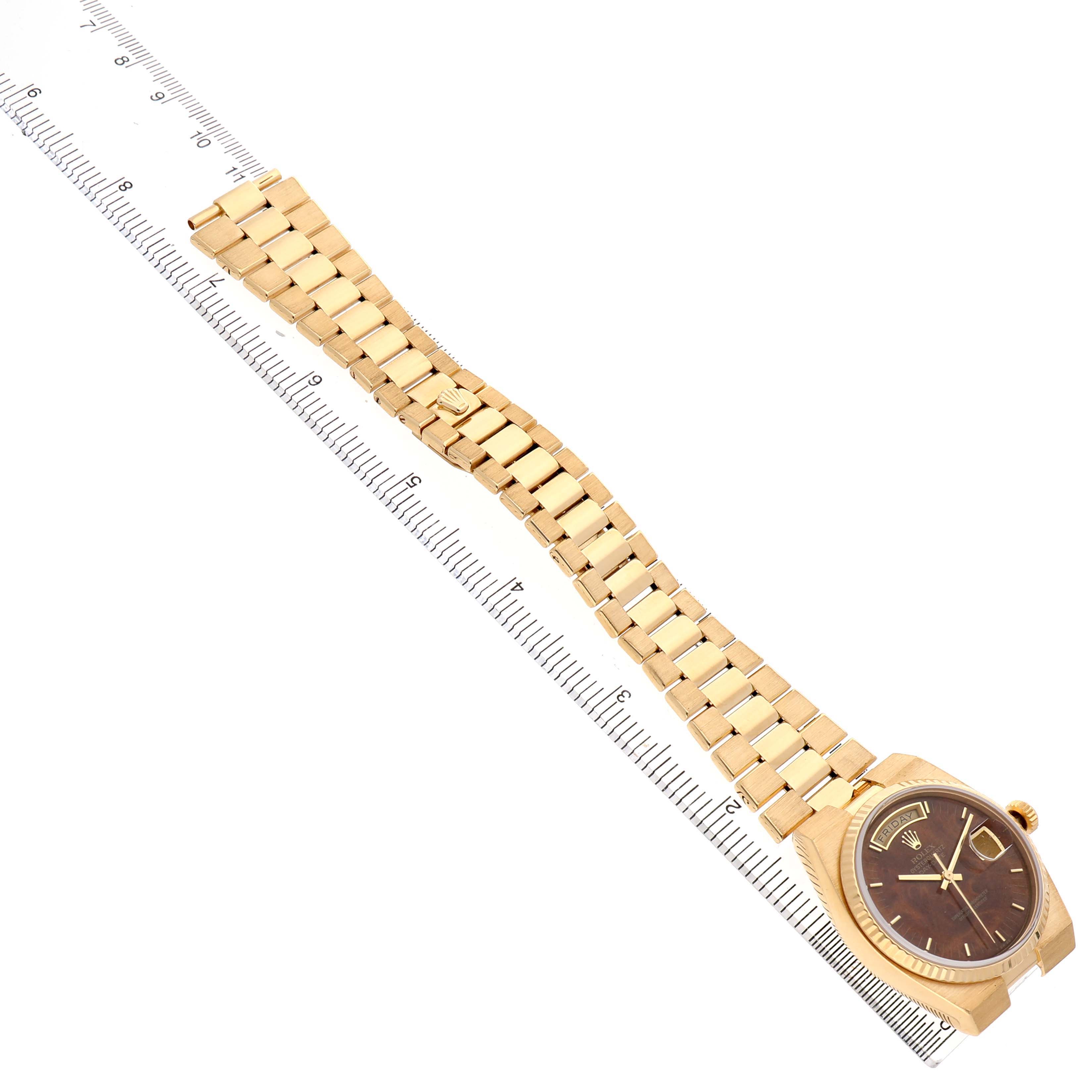 The Rolex Oysterquartz 19018 Men's Yellow Gold Brown Dial watch is shown from a top view, featuring the entire watch band and the case beside a ruler.