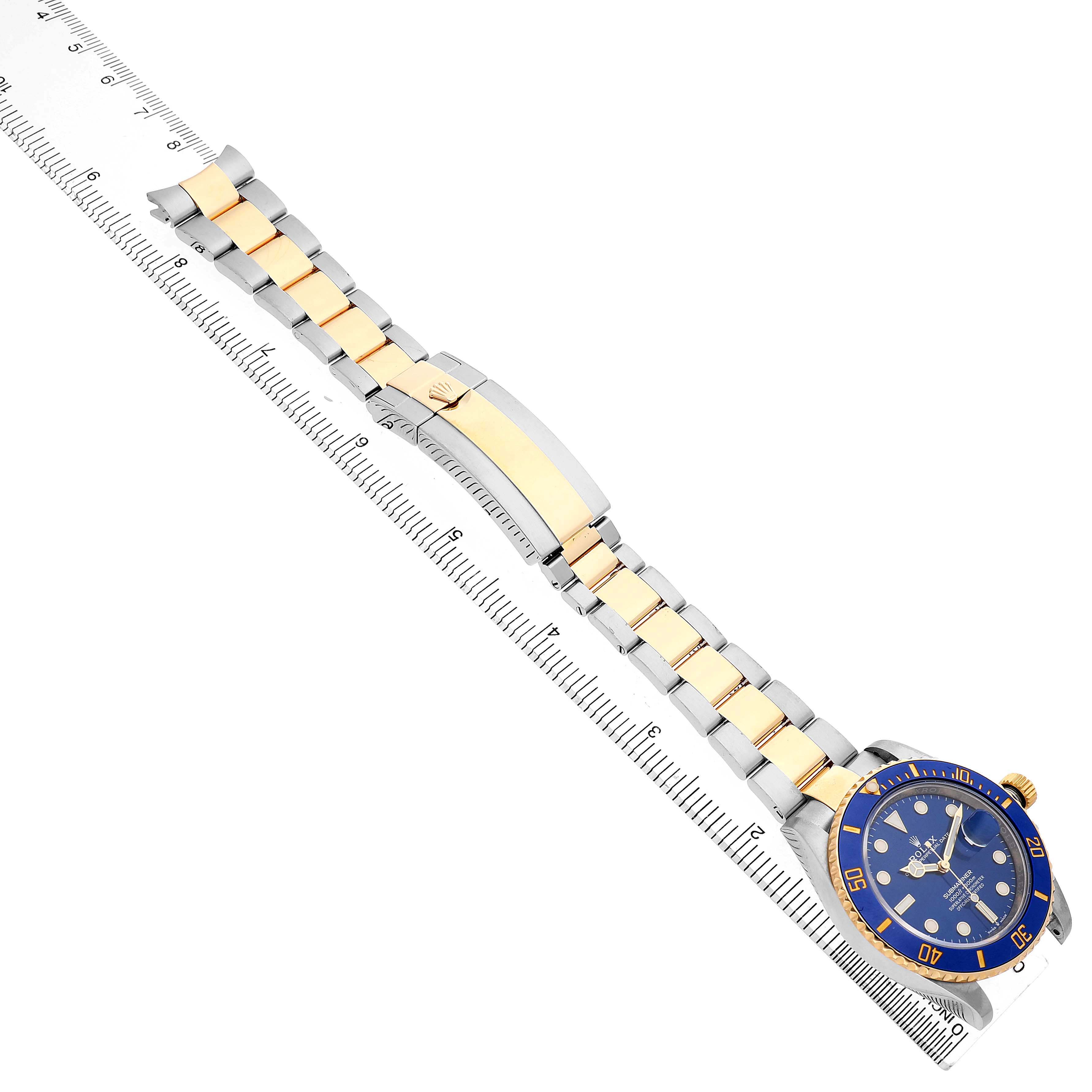The Rolex Submariner 126613 Men's Steel and Gold (two tone) Blue Dial watch is shown from an overhead angle, highlighting the bracelet, clasp, and face against a measuring ruler.