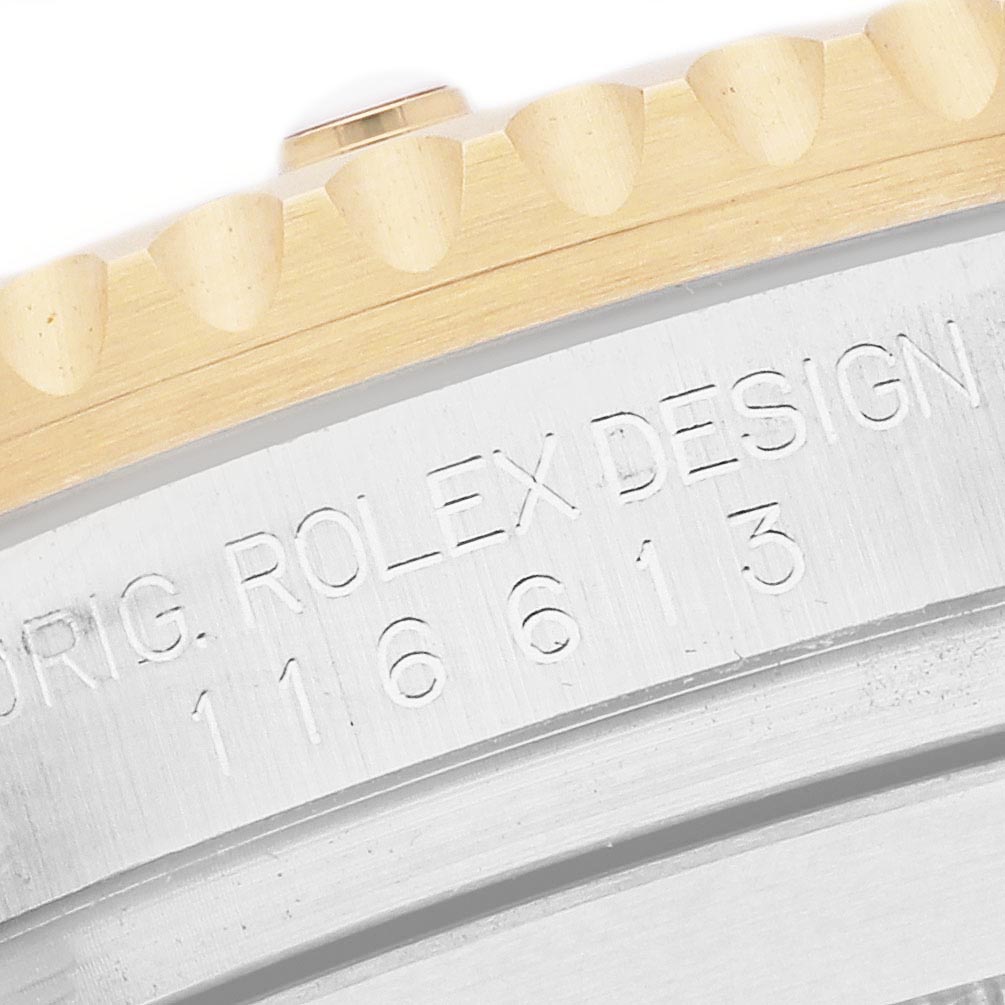 The image shows a close-up of the side of a Rolex Submariner 116613 Men
s Steel and Gold (two tone) Blue Dial 116613 Men
s Steel and Gold (two tone) Blue Dial, focusing on the bezel teeth and engraved serial number.