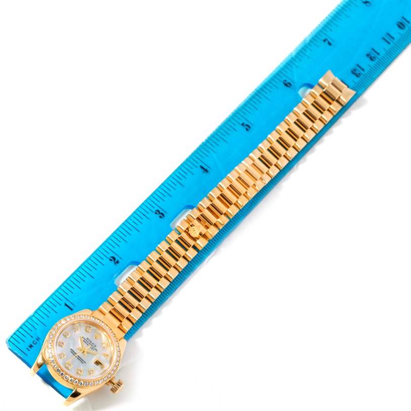 The image shows a Rolex President 179138 Women's Yellow Gold Mother of Pearl Dial 179138 Women's Yellow Gold Mother of Pearl Dial model watch placed against a blue ruler, displaying the watch face and full gold bracelet.