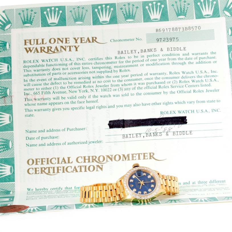 The image shows a Rolex President 69178 Women's Yellow Gold Blue Dial 69178 Women's Yellow Gold Blue Dial model watch with a gold bracelet, placed on top of its official warranty and chronometer certification papers.