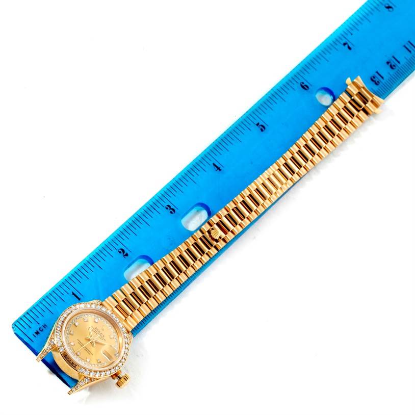 The Rolex President 69158 Women's Yellow Gold Champagne Dial 69158 Women's Yellow Gold Champagne Dial model watch is shown from above, displaying the dial, crown, and bracelet next to a blue ruler.