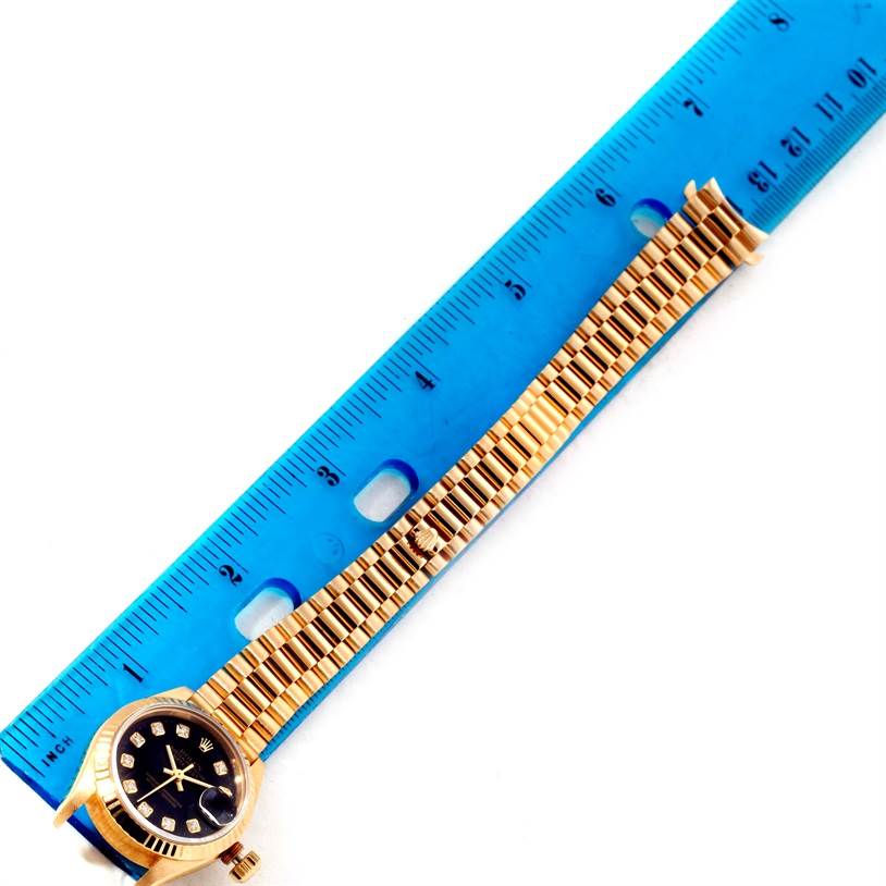This image shows a President model Rolex watch with a blue ruler measuring its gold band length.