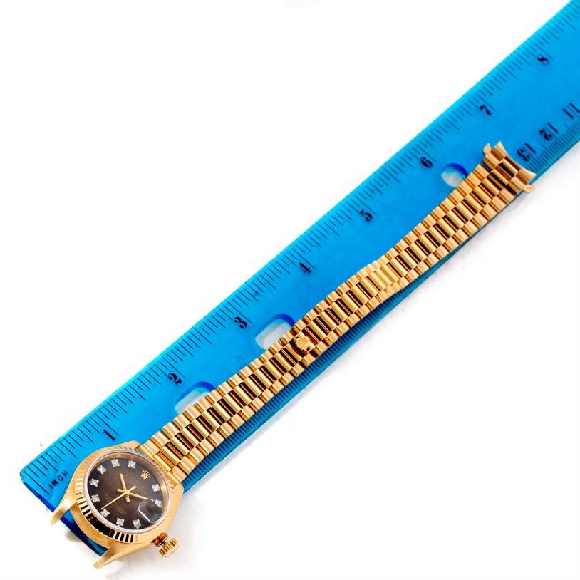 The Rolex President 69178 Women's Yellow Gold Brown Dial 69178 Women's Yellow Gold Brown Dial model watch is shown from a top-down angle, displaying its face and band alongside a ruler for scale.