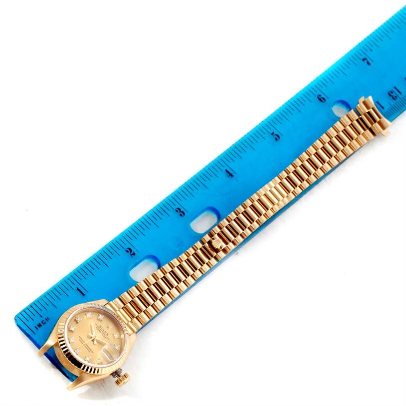 The image shows an overhead view of a Rolex President 69178 Women's Yellow Gold Champagne Dial 69178 Women's Yellow Gold Champagne Dial model watch with its bracelet next to a ruler for scale.