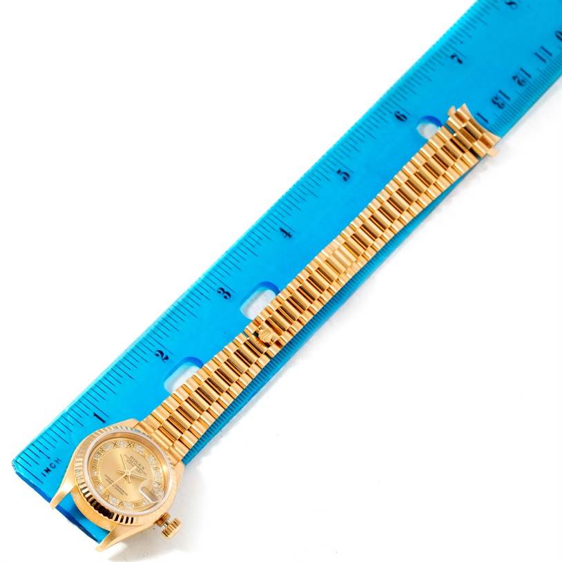 The Rolex President 69178 Women's Yellow Gold Champagne Dial 69178 Women's Yellow Gold Champagne Dial watch is shown from a top-down angle, displaying its gold bracelet and face next to a blue ruler.