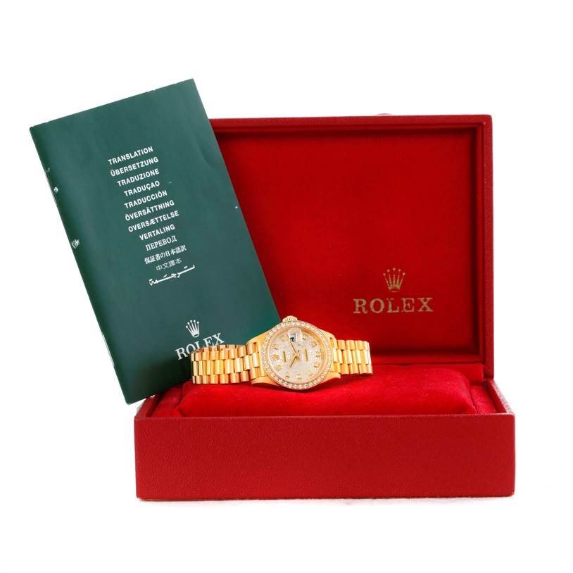 The image shows the Rolex President 69138 Women's Yellow Gold Beige Dial 69138 Women's Yellow Gold Beige Dial model watch and its bracelet inside a red Rolex box with a green booklet.