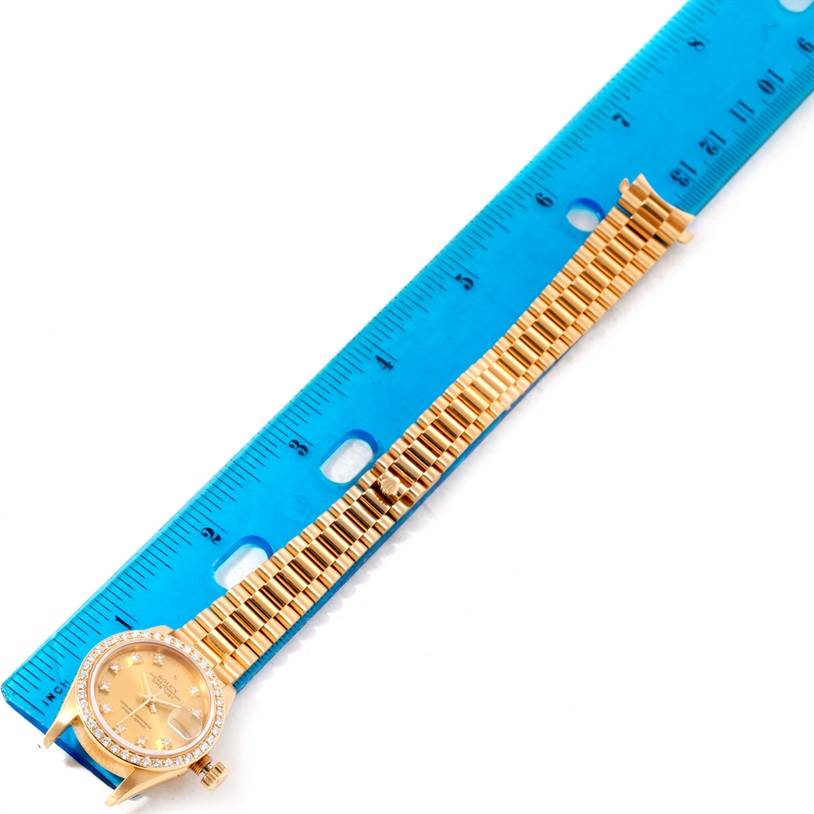 The image shows a President model by Rolex laid flat next to a blue ruler, displaying its dial and bracelet.