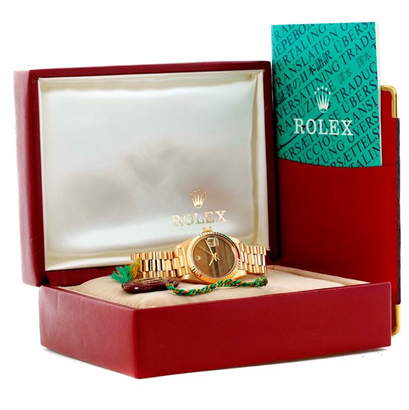 The image shows a Rolex President 6917 Women's Yellow Gold Brown Dial 6917 Women's Yellow Gold Brown Dial model watch and its accessories in an open red box with manuals on the side.