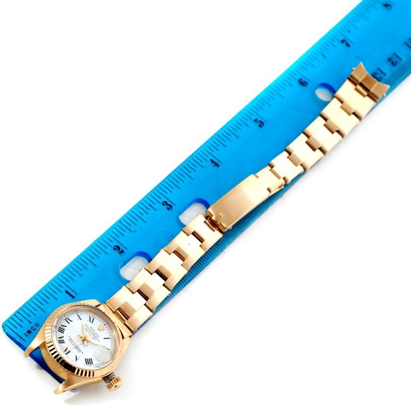 The image shows a Rolex President 6917 Women's Yellow Gold White Dial 6917 Women's Yellow Gold White Dial model watch laying flat next to a blue ruler, highlighting its band and watch face.