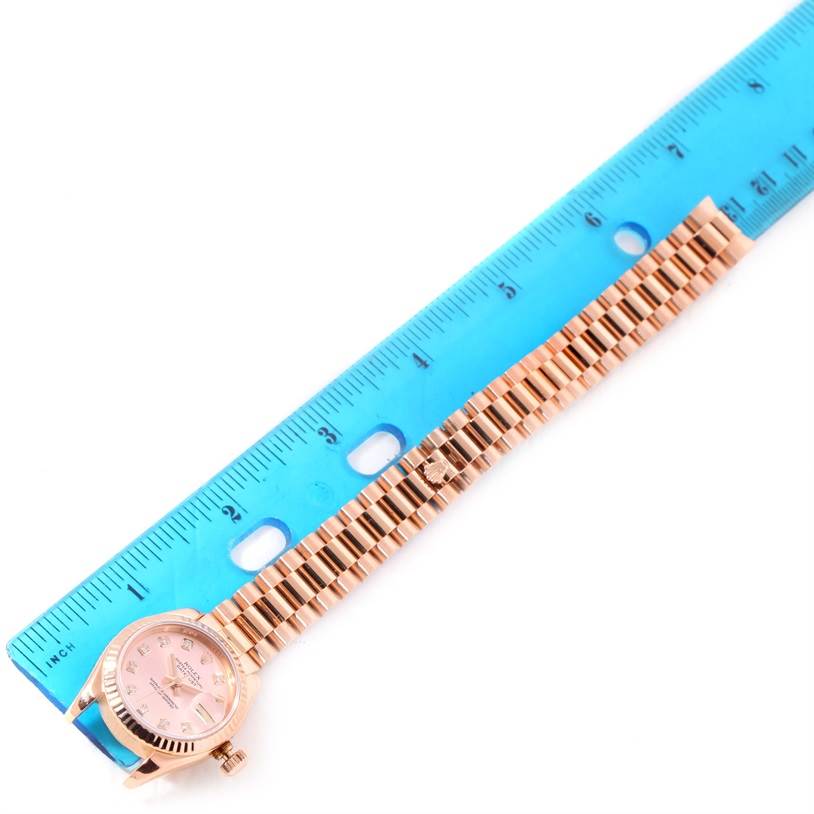 This image shows a Rolex President 179175 Women's Rose Gold Pink Dial 179175 Women's Rose Gold Pink Dial model watch with a laid-out bracelet next to a blue ruler for size comparison.