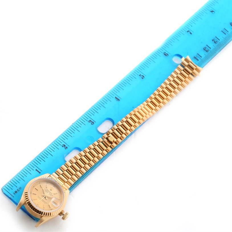 This image shows a Rolex President 69178 Women's Yellow Gold Champagne Dial 69178 Women's Yellow Gold Champagne Dial model watch laid flat next to a blue ruler, highlighting the watch face and part of the bracelet.