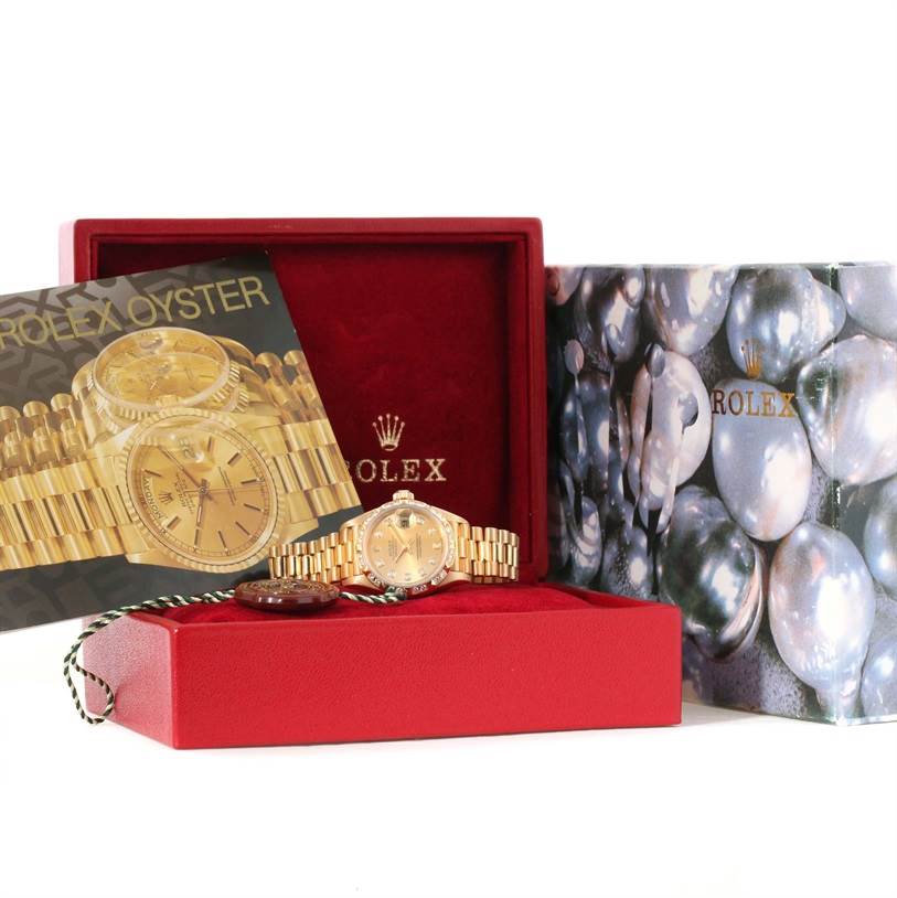 This image shows a Rolex President 79258 Women's Yellow Gold Champagne Dial 79258 Women's Yellow Gold Champagne Dial model watch, its box, and accompanying booklet from a frontal angle.