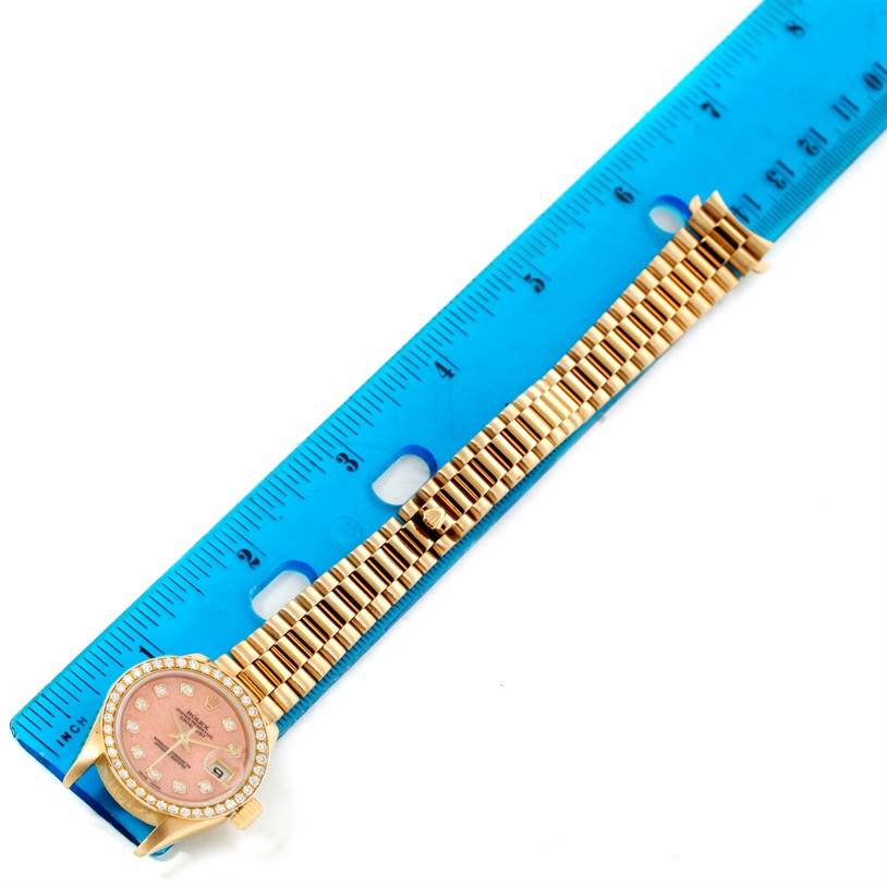 The Rolex President 69138 Women
s Yellow Gold Pink Dial 69138 Women
s Yellow Gold Pink Dial watch is shown from a top view, displaying its face and bracelet next to a blue ruler for scale.