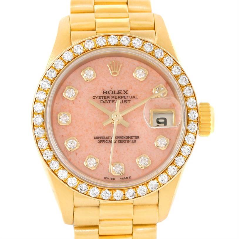 This image shows a Rolex President 69138 Women
s Yellow Gold Pink Dial 69138 Women
s Yellow Gold Pink Dial model watch from a front angle, highlighting its pink dial, date window, and diamond bezel.