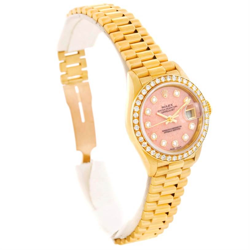 The image shows a side angle of a Rolex President 69138 Women
s Yellow Gold Pink Dial 69138 Women
s Yellow Gold Pink Dial model watch, highlighting the pink dial, diamond bezel, and gold bracelet.