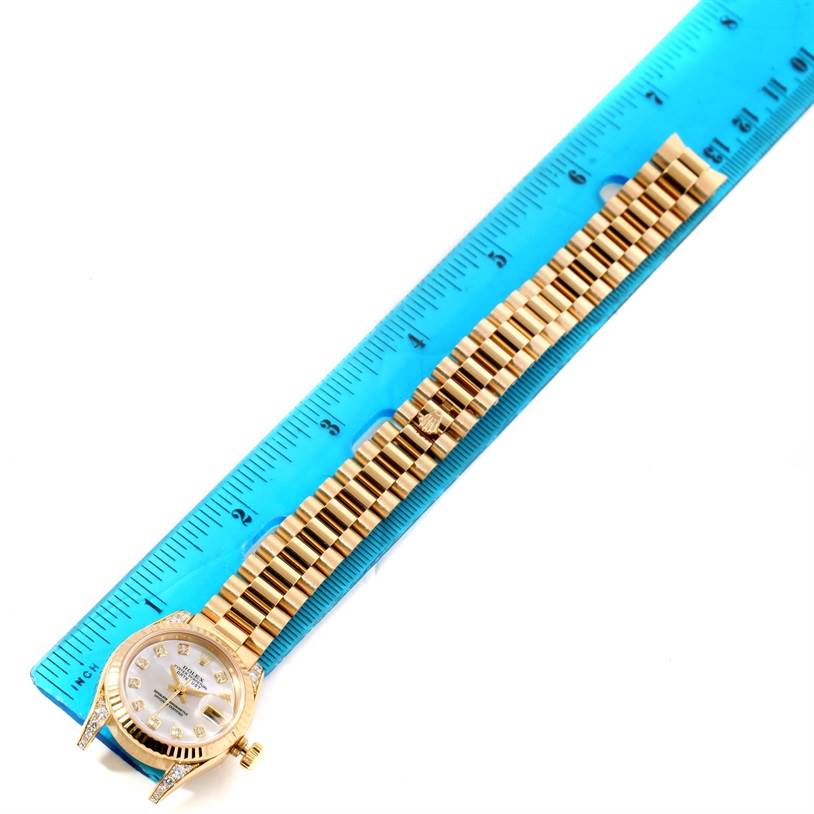 The image shows a Rolex President 179238 Women
s Yellow Gold Mother of Pearl Dial 179238 Women
s Yellow Gold Mother of Pearl Dial model watch laid flatly along a blue ruler, displaying its face and full gold bracelet.