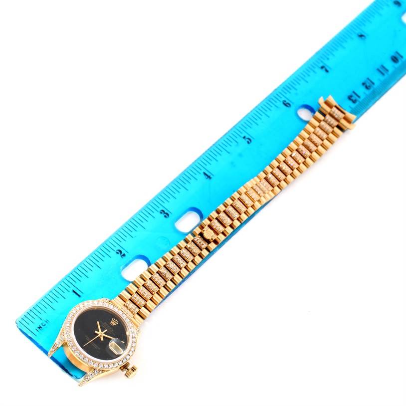 The Rolex President 69158 Women's Yellow Gold Black Dial 69158 Women's Yellow Gold Black Dial model watch is shown lying flat next to a blue ruler, displaying the face and band.