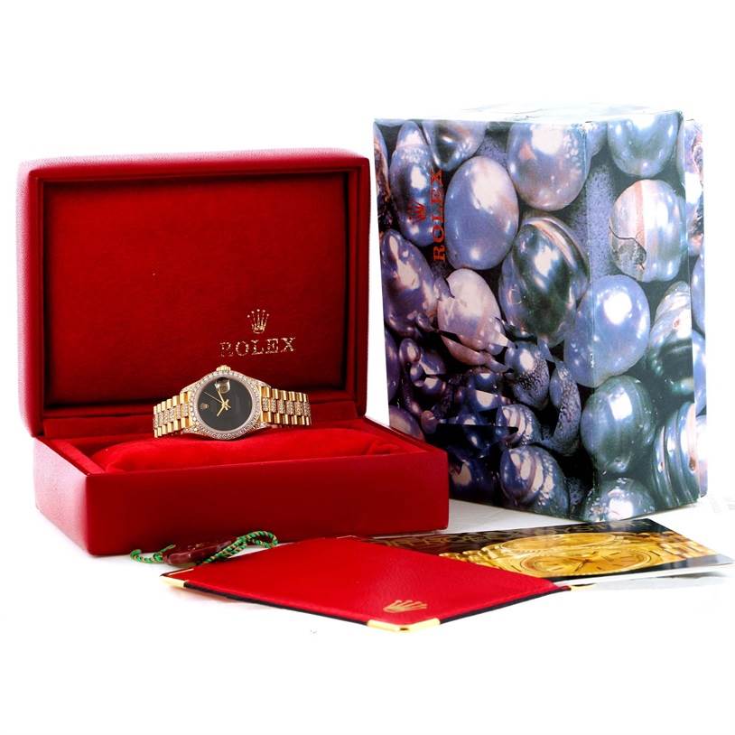 The Rolex President 69158 Women's Yellow Gold Black Dial 69158 Women's Yellow Gold Black Dial model watch is shown in an open red box with its packaging and accessories around it.