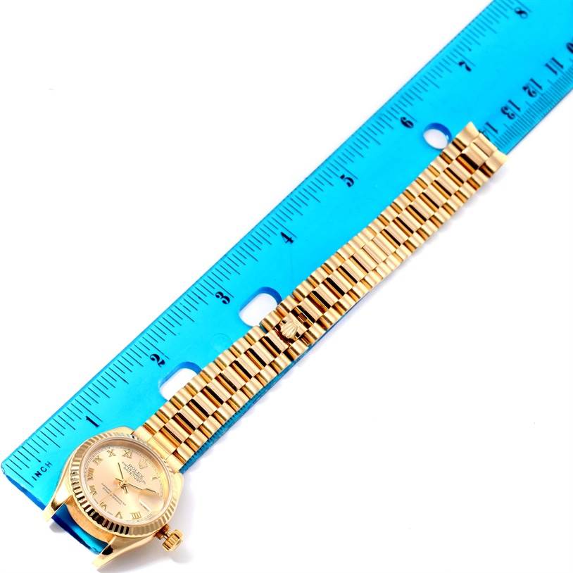 The image shows a Rolex President 179178 Women's Yellow Gold Champagne Dial 179178 Women's Yellow Gold Champagne Dial watch placed next to a blue ruler, highlighting the entire band and face.