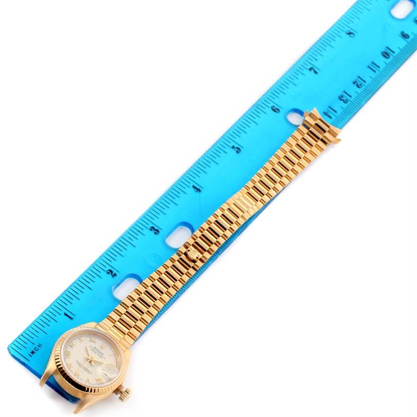 The image shows a President model Rolex watch laid flat next to a ruler, displaying its face and entire band.