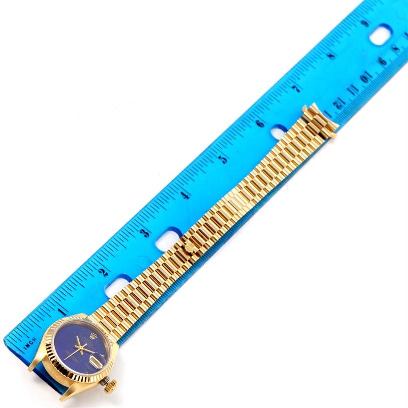 The image shows the Rolex President 69178 Women's Yellow Gold Blue Dial 69178 Women's Yellow Gold Blue Dial watch lying flat with its blue dial and gold bracelet fully extended alongside a blue ruler.
