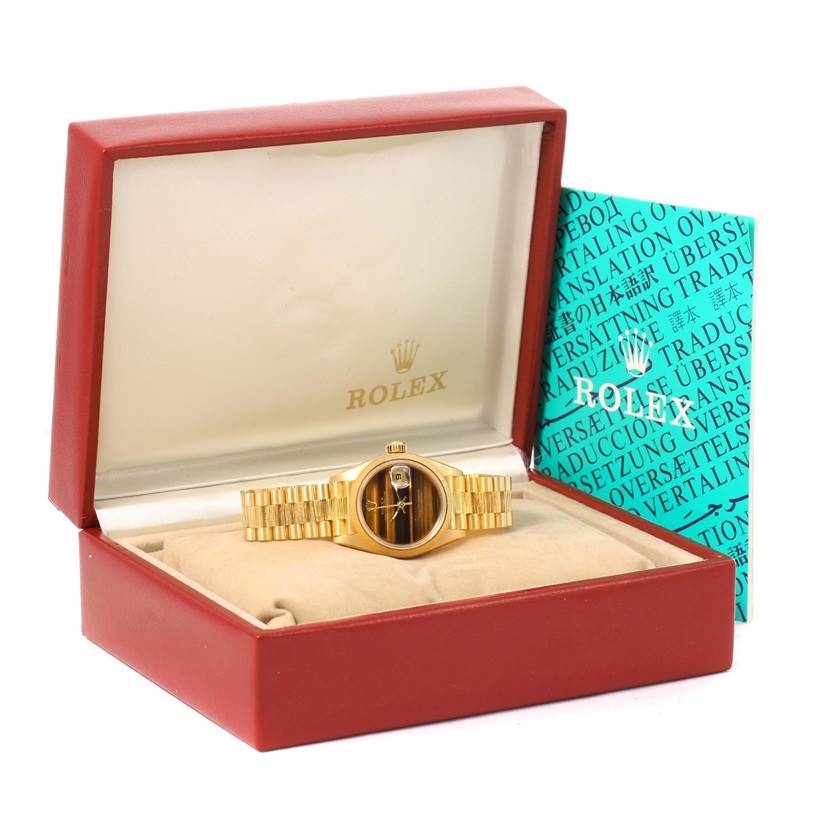 The image shows a Rolex President 69278 Women's Yellow Gold Brown Dial 69278 Women's Yellow Gold Brown Dial watch with a gold bracelet in an open red and beige Rolex box, alongside a turquoise document.