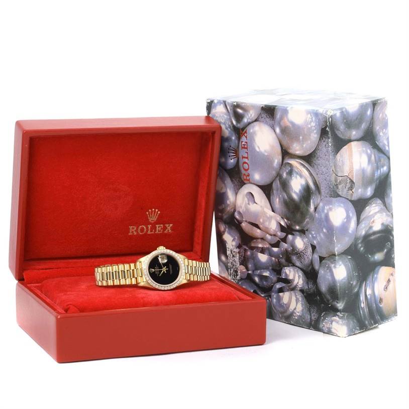 The Rolex President 69178 Women's Yellow Gold Black Dial 69178 Women's Yellow Gold Black Dial model watch is shown in its red box with a pearl-themed exterior box in the background.