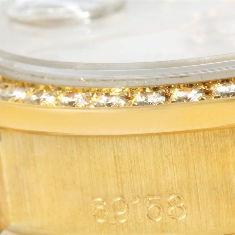 Close-up view of a Rolex President 69158 Women's Yellow Gold Silver Dial 69158 Women's Yellow Gold Silver Dial model watch showing its diamond-studded bezel and part of the case with engraved numbers.