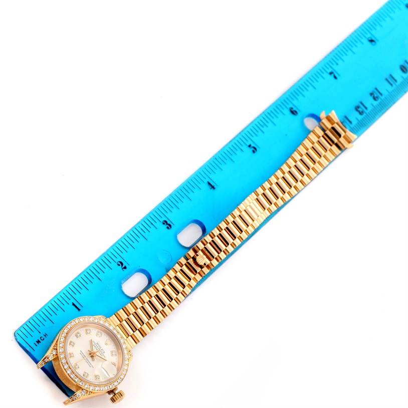 The image shows a Rolex President 69158 Women's Yellow Gold Silver Dial 69158 Women's Yellow Gold Silver Dial model watch lying flat next to a ruler, displaying the face and band.