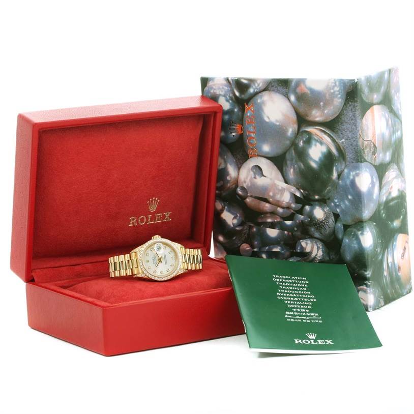 The Rolex President 69158 Women's Yellow Gold Silver Dial 69158 Women's Yellow Gold Silver Dial model watch is displayed in an open red box, with the original packaging and a green booklet beside it.