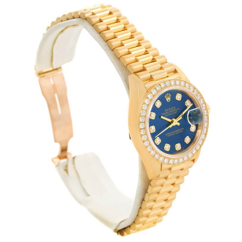 The image shows a side angle of a Rolex President 69138 Women's Yellow Gold Blue Dial 69138 Women's Yellow Gold Blue Dial model watch, highlighting its gold band, blue dial, and diamond-encrusted bezel.