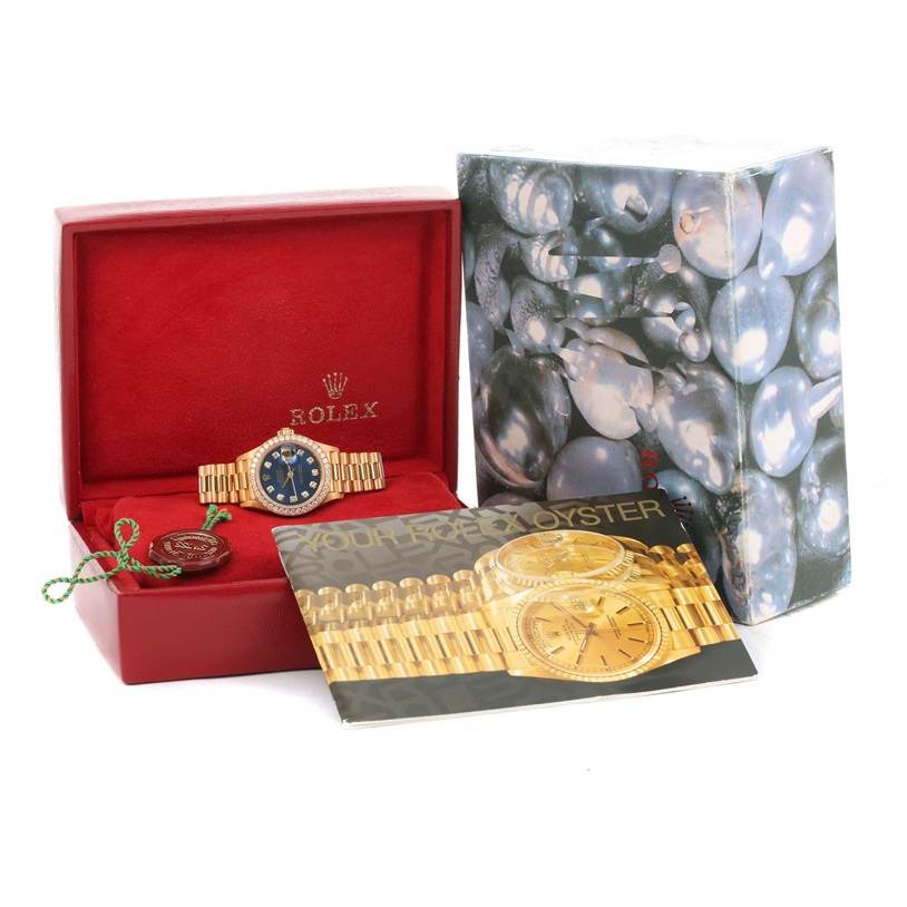 A Rolex President 69138 Women's Yellow Gold Blue Dial 69138 Women's Yellow Gold Blue Dial model watch is displayed in its open box, accompanied by branding material and a decorative outer box.