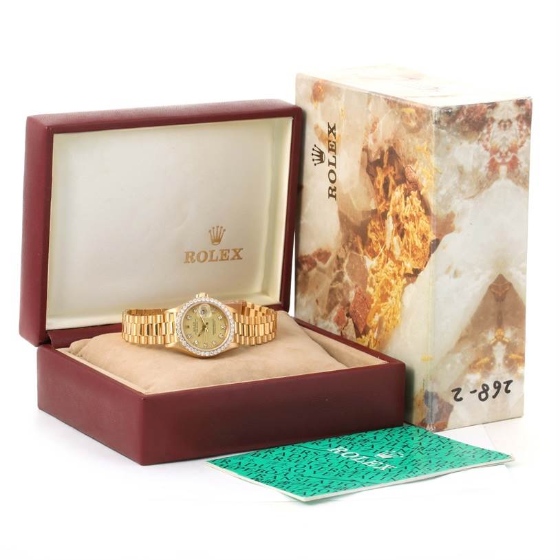 The image shows a Rolex President 69178 Women's Yellow Gold Champagne Dial 69178 Women's Yellow Gold Champagne Dial model watch, positioned in its open box with packaging and documents beside it.