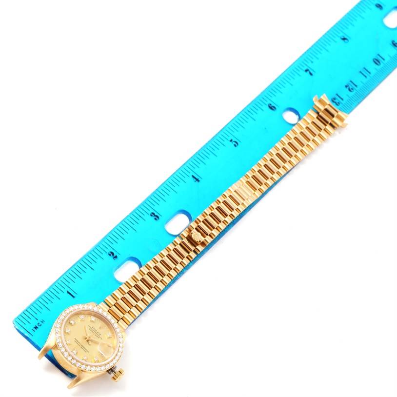 The image shows the Rolex President 69178 Women's Yellow Gold Champagne Dial 69178 Women's Yellow Gold Champagne Dial model watch lying flat next to a blue ruler, displaying its gold band and bezel.