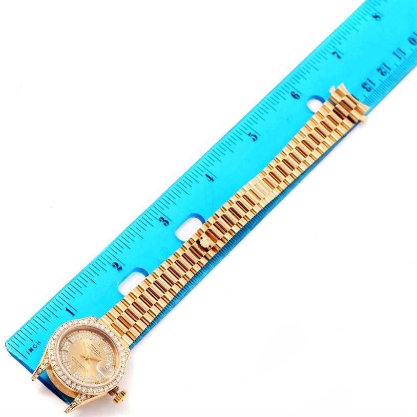 This image shows a Rolex President 69188 Women's Yellow Gold Champagne Dial 69188 Women's Yellow Gold Champagne Dial model watch laid next to a blue ruler, highlighting the watch face and band.