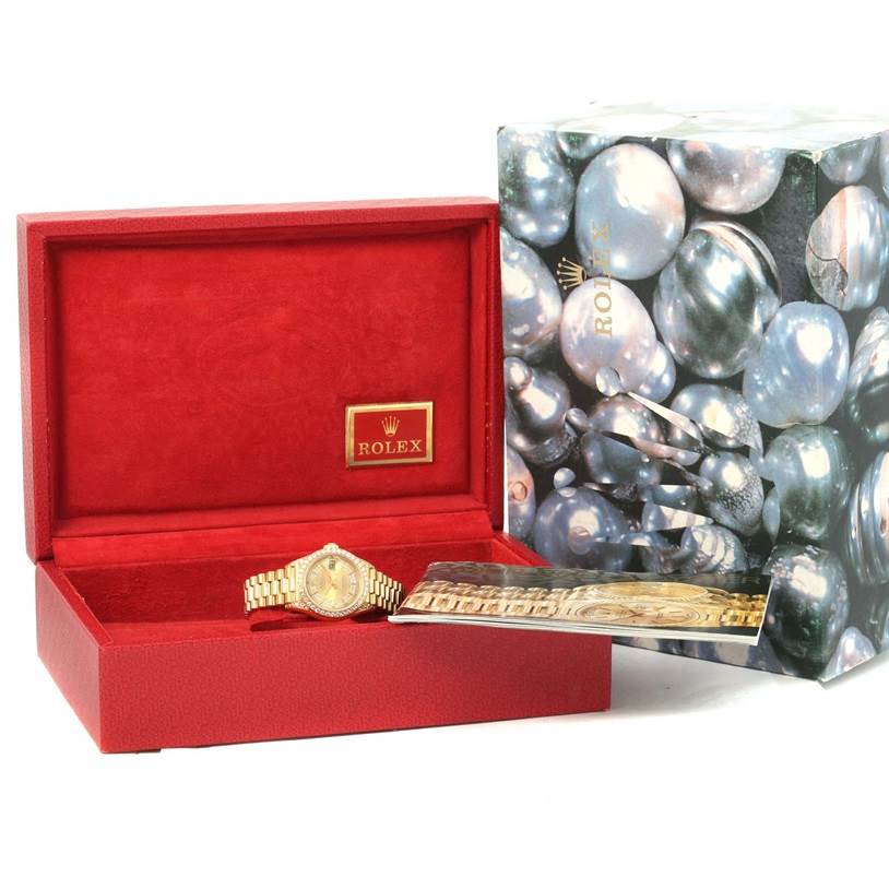 The Rolex President 69188 Women's Yellow Gold Champagne Dial 69188 Women's Yellow Gold Champagne Dial model watch is displayed in an open red box, with its booklet and an outer box featuring pearl imagery.