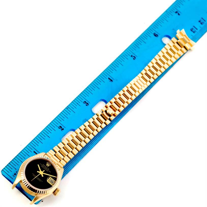 This image shows the Rolex President 69178 Women's Yellow Gold Black Dial 69178 Women's Yellow Gold Black Dial model watch placed next to a blue ruler, displaying the watch face, bezel, and band.