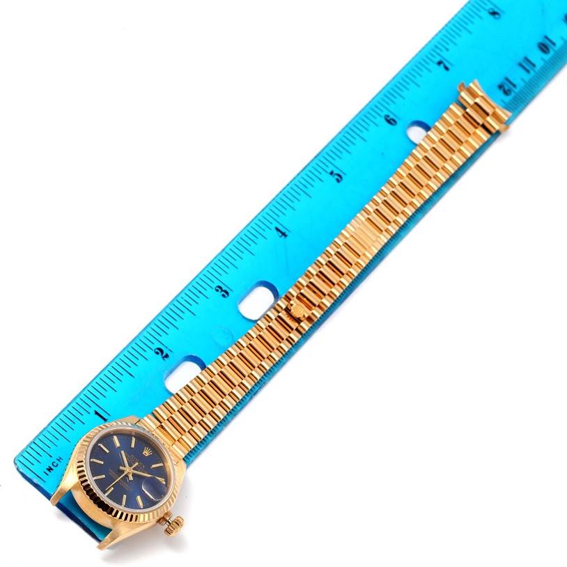 The image shows a side angle of a Rolex President 69178 Women's Yellow Gold Blue Dial 69178 Women's Yellow Gold Blue Dial model watch with its band laid alongside a ruler for measurement.