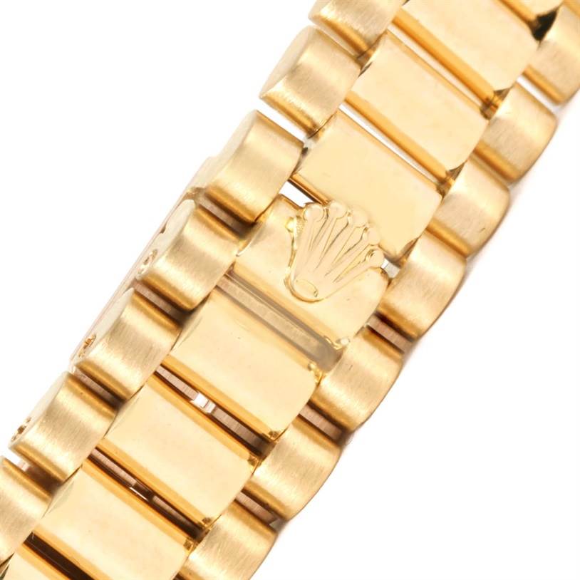This image shows a close-up of the gold President bracelet of a Rolex watch, highlighting Rolex's crown logo on the clasp.