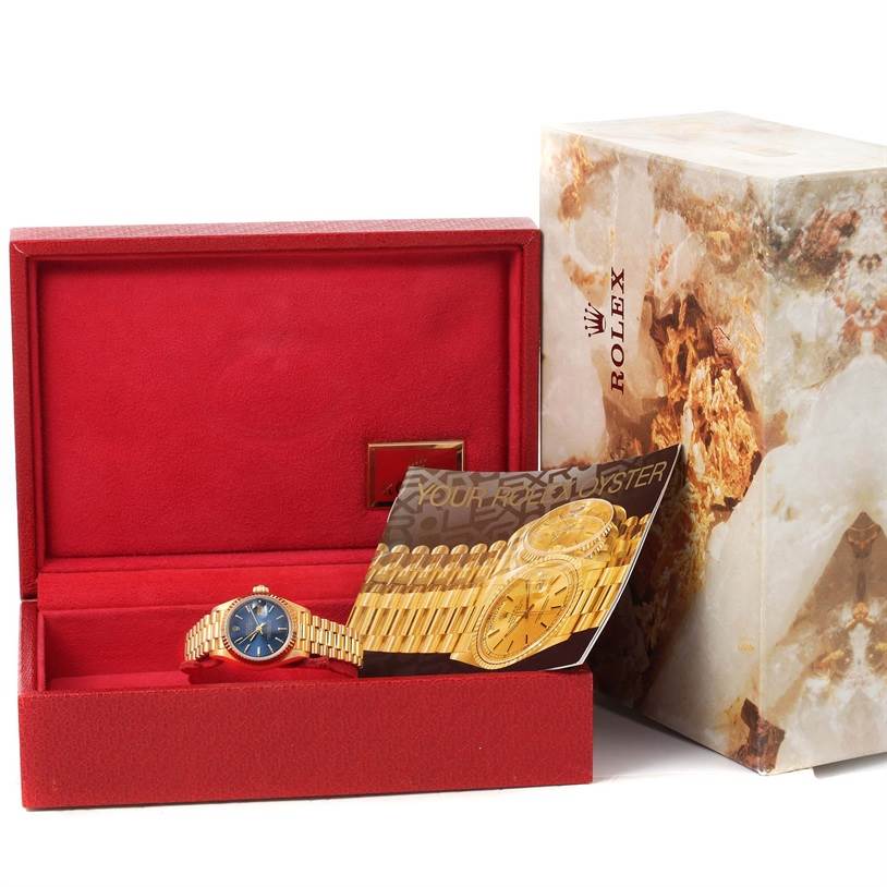 The image shows a Rolex President 69178 Women's Yellow Gold Blue Dial 69178 Women's Yellow Gold Blue Dial model watch from a front angle, displayed in an open red box with accompanying booklets.
