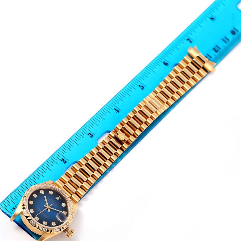 The image shows a Rolex President 68258 Women's Yellow Gold Blue Dial 68258 Women's Yellow Gold Blue Dial model watch next to a blue ruler, focusing on the bracelet and face.