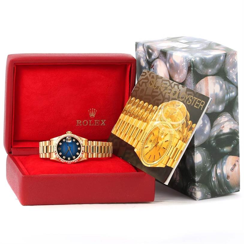 The image shows a Rolex President 68258 Women's Yellow Gold Blue Dial 68258 Women's Yellow Gold Blue Dial model watch in its red box with its booklet and outer box.